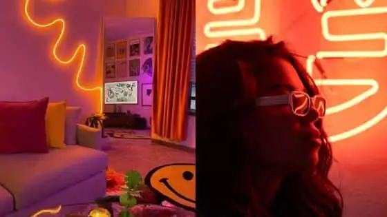 Vibrant room with neon lighting and smiley decor; woman in glasses illuminated by red neon light. Cozy, modern ambiance.