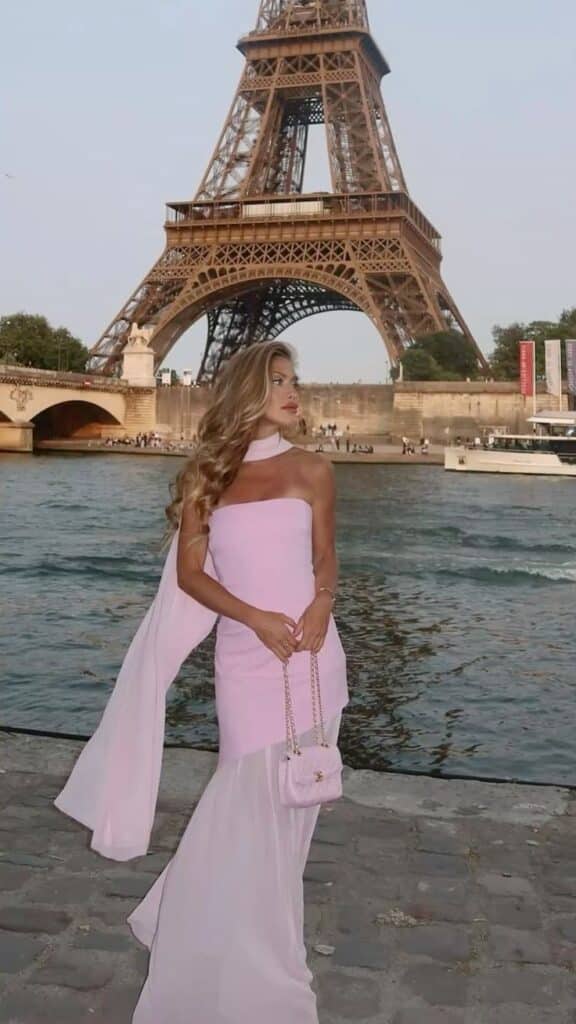 Insta_majamalnar Woman in pink dress poses by Eiffel Tower, Paris, with calm river in background. Elegant fashion and iconic landmark scene. | Sky Rye Design Woman in pink dress poses by Eiffel Tower, Paris, with calm river in background. Elegant fashion and iconic landmark scene.