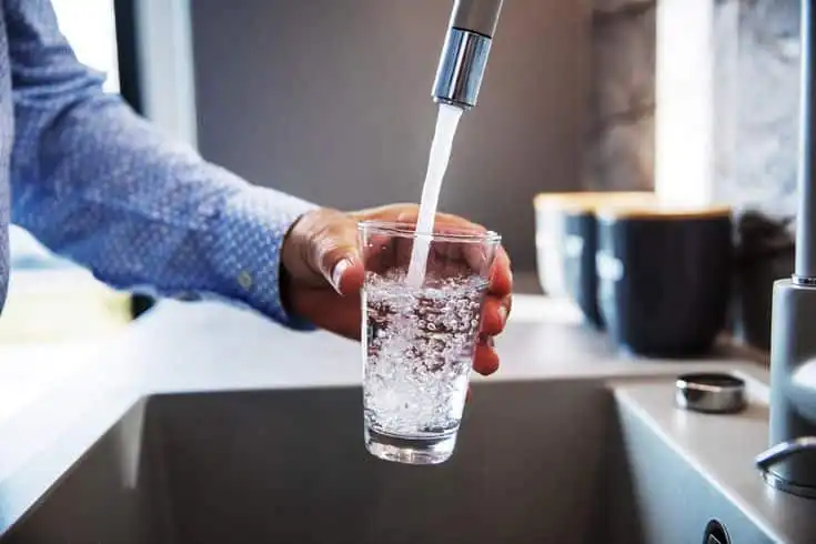 Close-up of a hand filling a glass with clear water from a kitchen faucet, highlighting fresh and clean hydration at home.