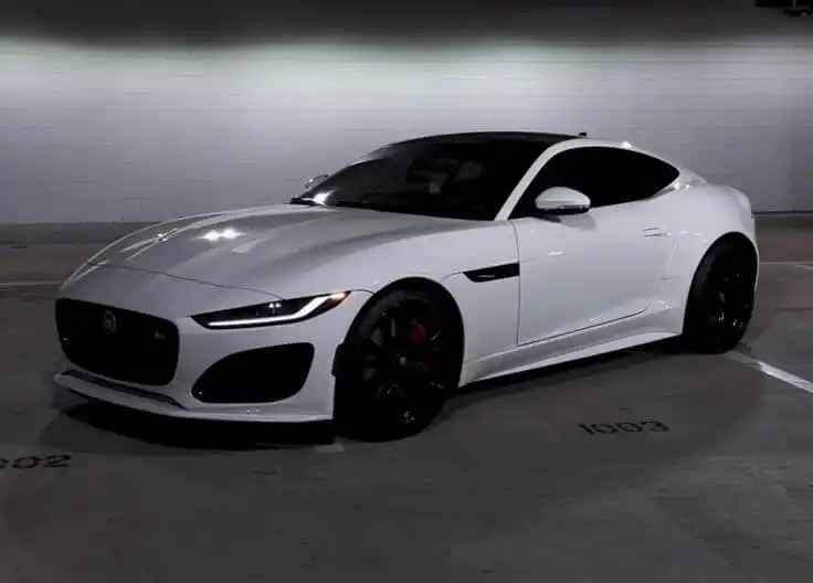 Sleek white sports car parked in a dimly lit garage, showcasing modern design and aerodynamic curves. who is jaguar owned by