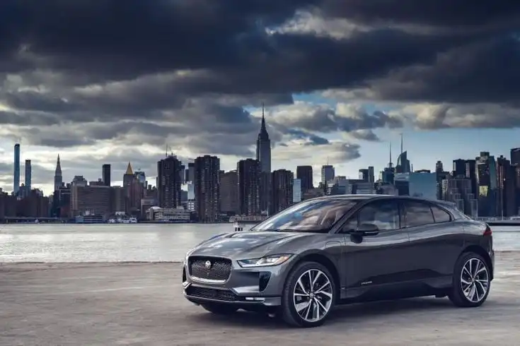 Sleek gray SUV parked near waterfront with a skyline backdrop under dramatic clouds, showcasing modern urban elegance and