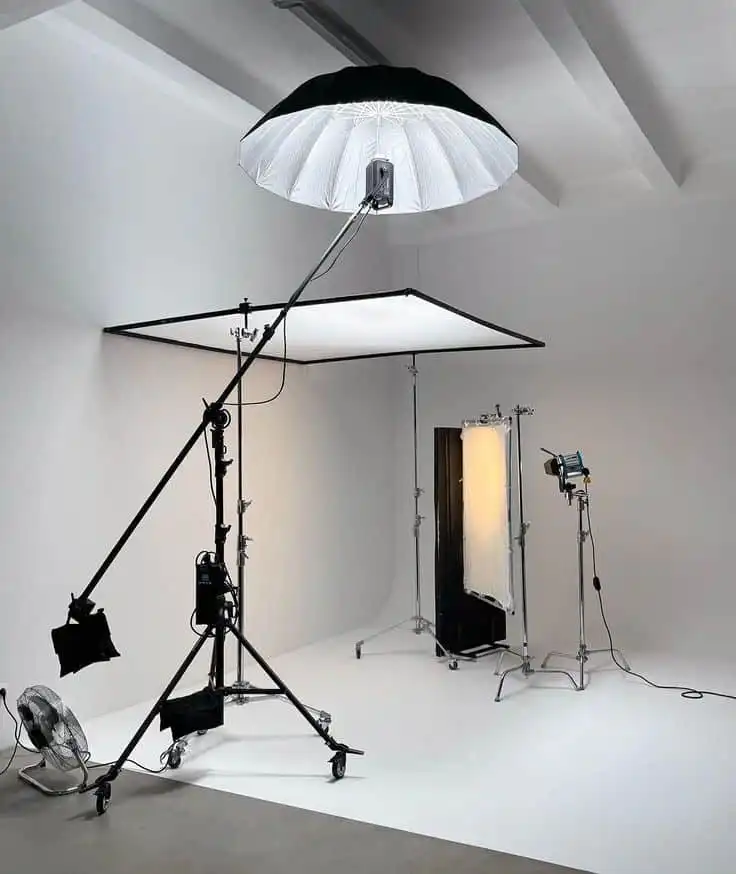 Photography studio setup with professional lighting equipment, including softboxes and reflectors, in a spacious white room.
