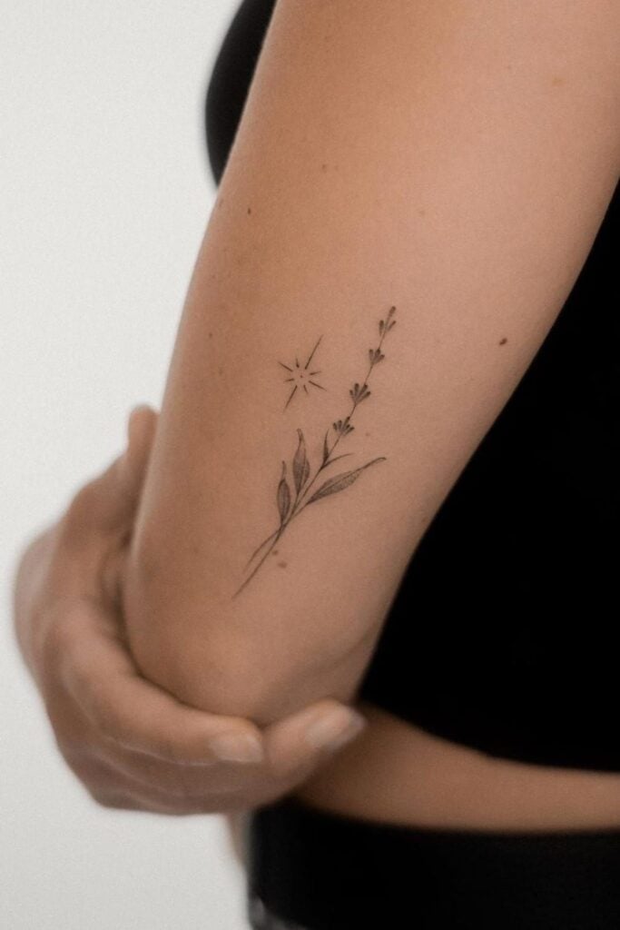 Minimalist floral tattoo on a person's arm, featuring delicate leaves and a small starburst design, highlighting simplicity and elegance.