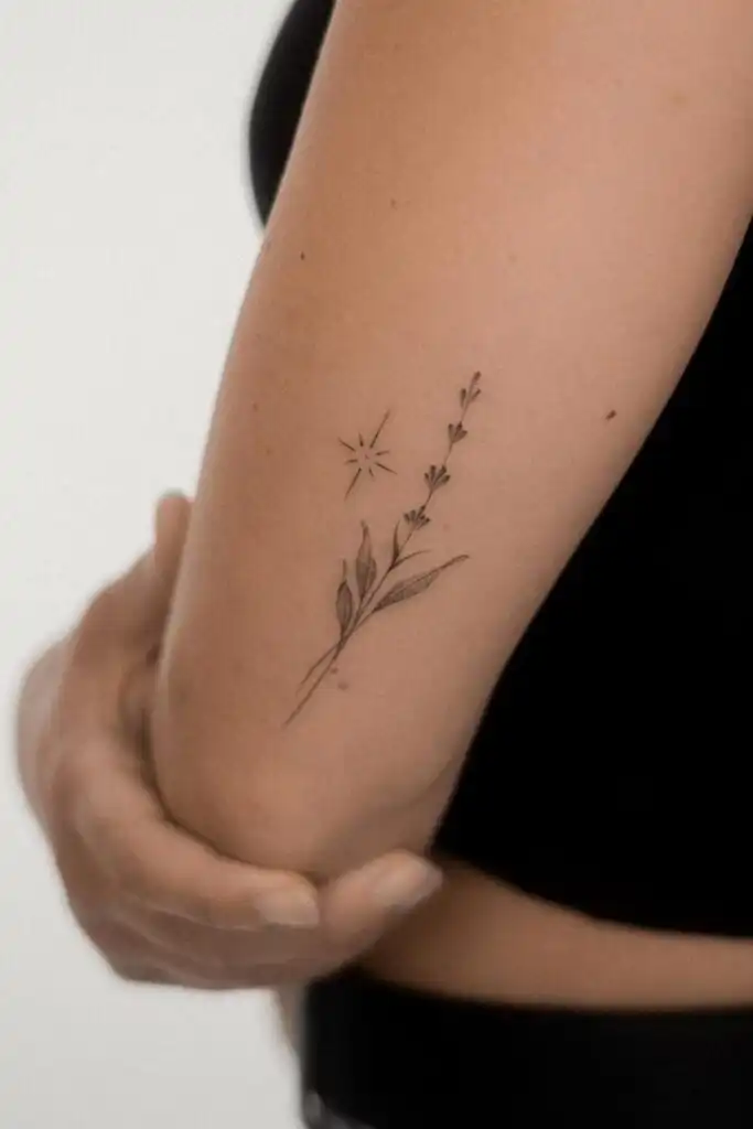 Minimalist floral tattoo on a person's arm, featuring delicate leaves and a small starburst design, highlighting simplicity and elegance.