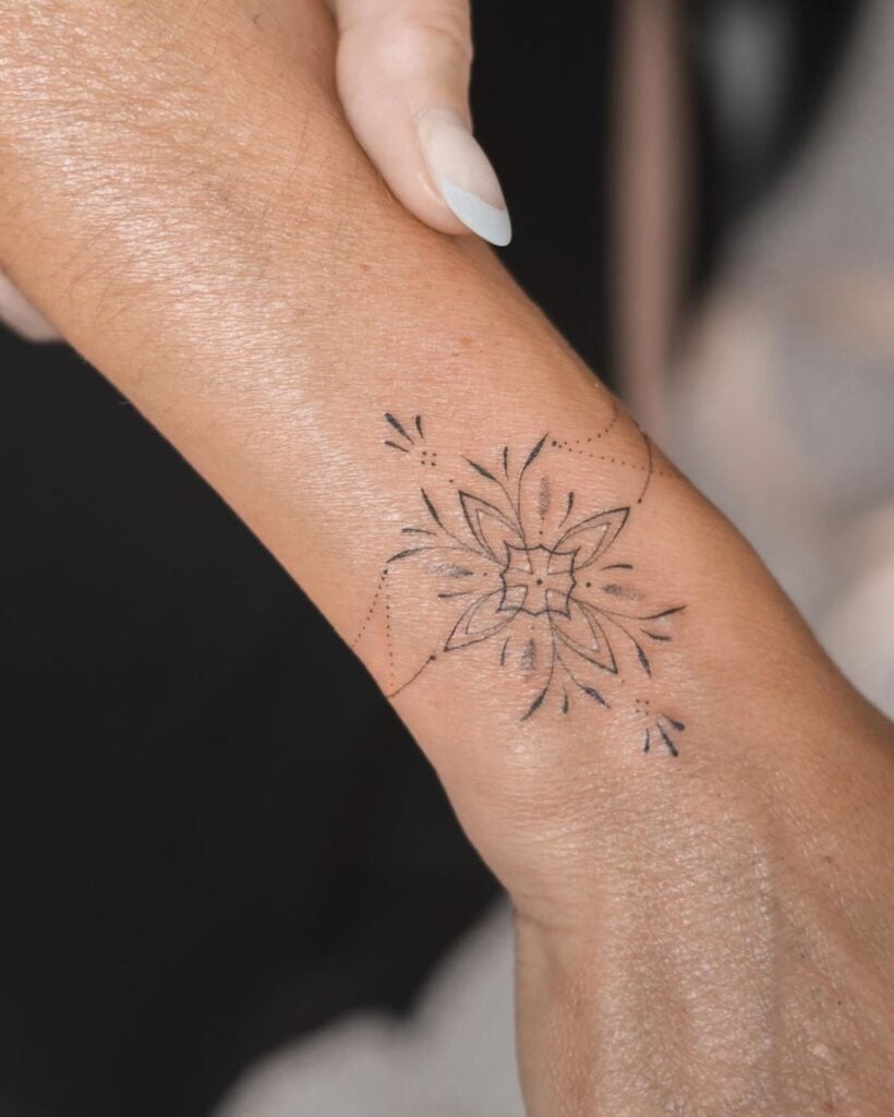 Intricate wrist tattoo featuring a symmetrical floral design with delicate linework, highlighting artistry and elegance on skin.