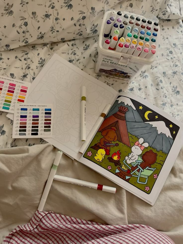 Mindful colouring Coloring book page with camping scene, surrounded by Ohuhu markers and color swatches on a floral bedspread. | Sky Rye Design Coloring book page with camping scene, surrounded by Ohuhu markers and color swatches on a floral bedspread.