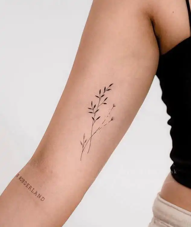 Delicate floral tattoo on a person's forearm featuring thin leafy branches, showcasing minimalist design.