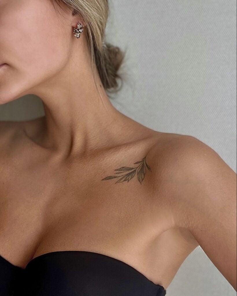 Woman with floral tattoo on shoulder, wearing butterfly earrings and strapless top, showcasing elegant and minimal style.