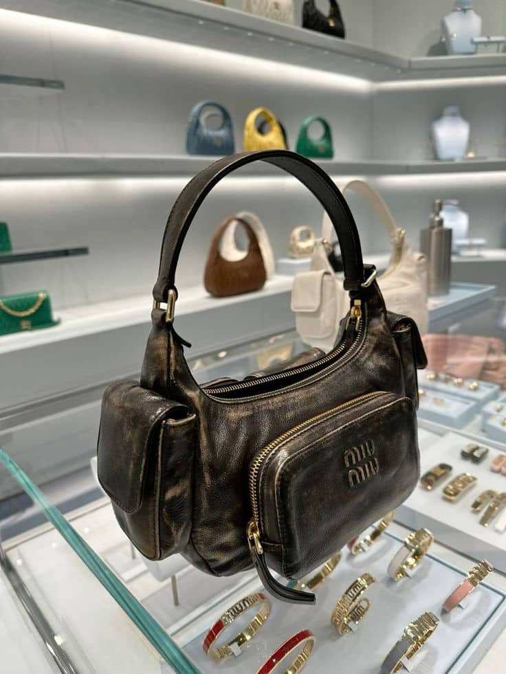 MiuMiu Bag Elegant black leather handbag on display with gold zipper detail, surrounded by various designer bags and accessories in a luxury store. | Sky Rye Design Elegant black leather handbag on display with gold zipper detail, surrounded by various designer bags and accessories in a luxury store.