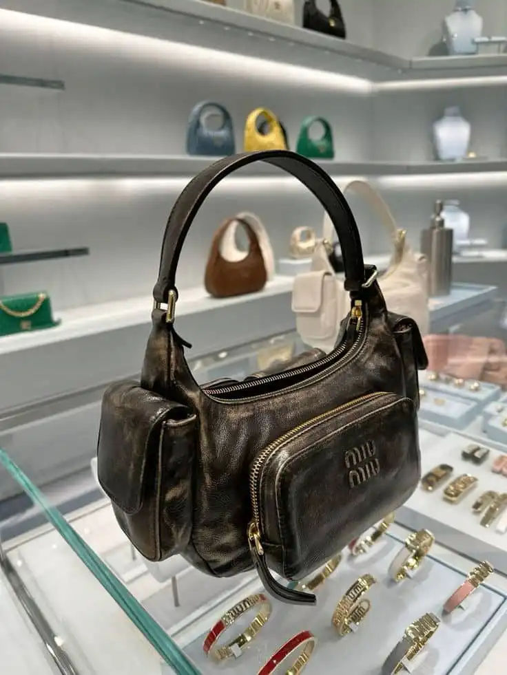 Elegant black leather handbag on display with gold zipper detail, surrounded by various designer bags and accessories in a luxury store.