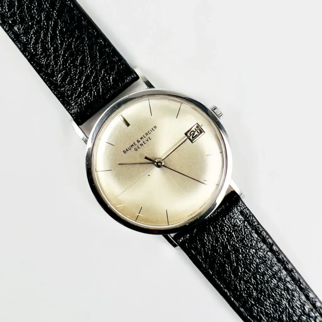 Vintage Baume & Mercier watch with a round dial and black leather strap, featuring a date display. Classic and elegant design.