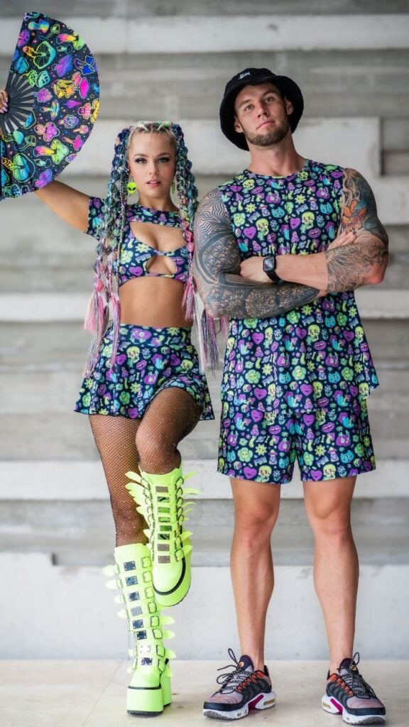 Neon Trip Cutout Kini Top Fashionable duo in vibrant matching outfits, one with neon boots, striking poses with a colorful fan against a neutral | Sky Rye Design Fashionable duo in vibrant matching outfits, one with neon boots, striking poses with a colorful fan against a neutral