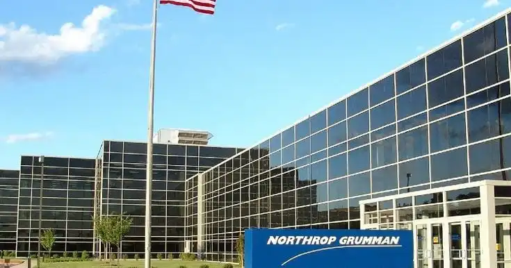 Modern glass-fronted Northrop Grumman building with an American flag in the foreground under a clear blue sky.