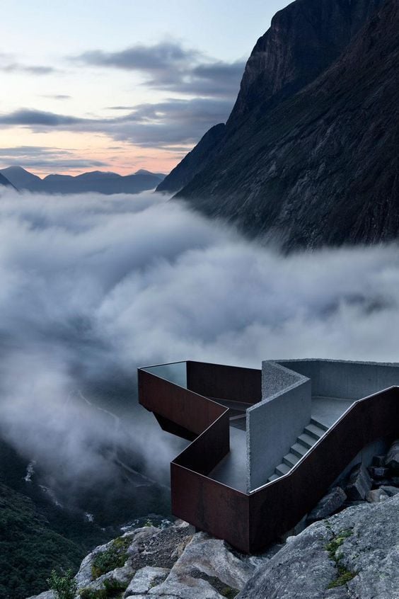 Dramatic viewing platform overlooking misty mountain landscape at sunrise, with clouds filling a deep valley. Breathtaking scenic view.
