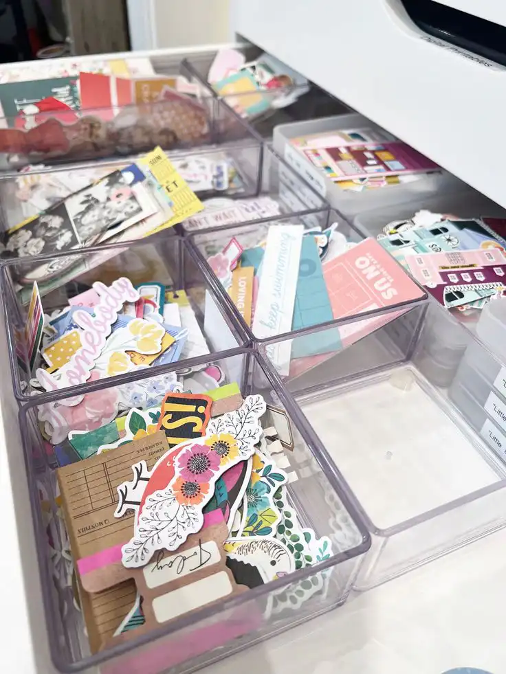 Organized craft supplies, stickers, and cutouts neatly stored in transparent drawer dividers, perfect for scrapbooking and creative projects. Beginner's Scrapbooking Guide
