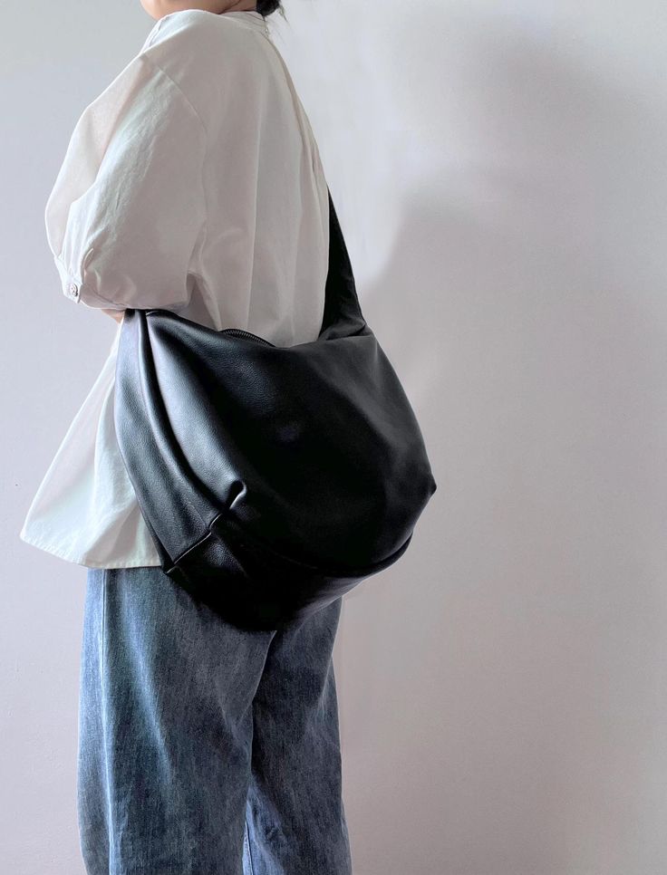 Person wearing a white shirt and jeans with a large black leather shoulder bag, perfect for casual and stylish everyday use.