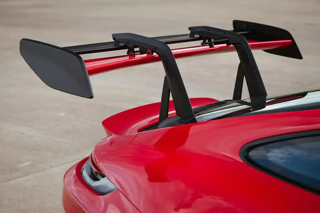 Red sports car rear view, featuring a prominent black spoiler for enhanced aerodynamics on a smooth concrete surface.