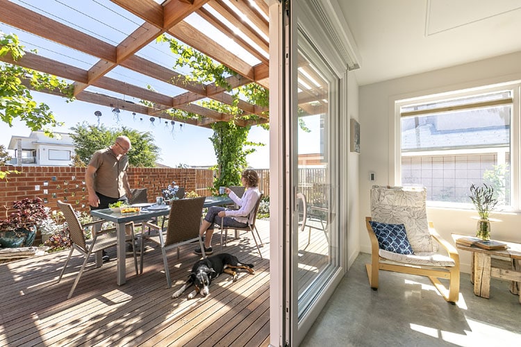 2 Wright ACT exterior 2 Sunlit patio with pergola, two people dining, and a dog resting, viewed from a bright interior room with a cozy chair. | Sky Rye Design Sunlit patio with pergola, two people dining, and a dog resting, viewed from a bright interior room with a cozy chair.