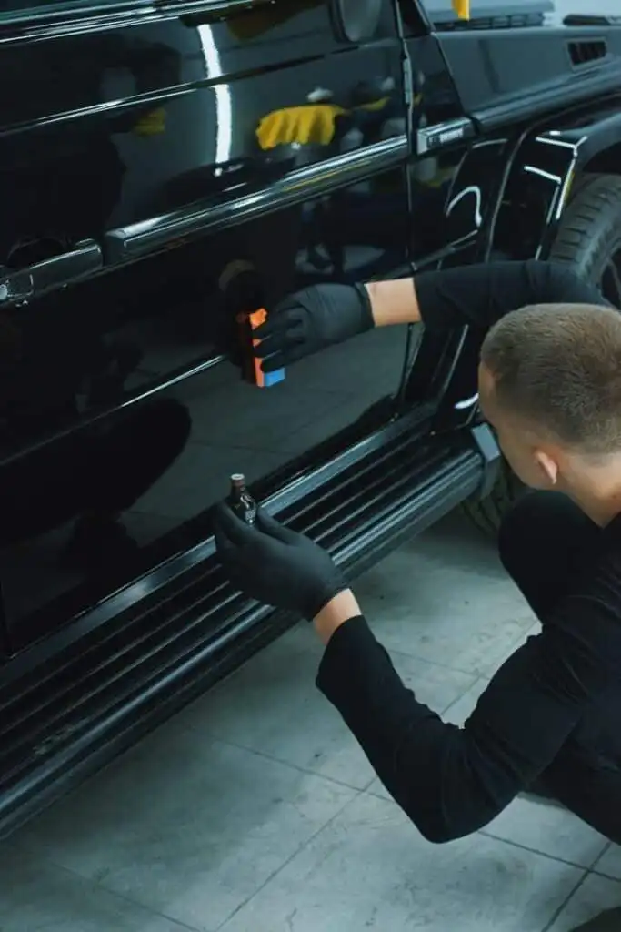 Man applying ceramic coating to black car door in garage, enhancing shine and protection.