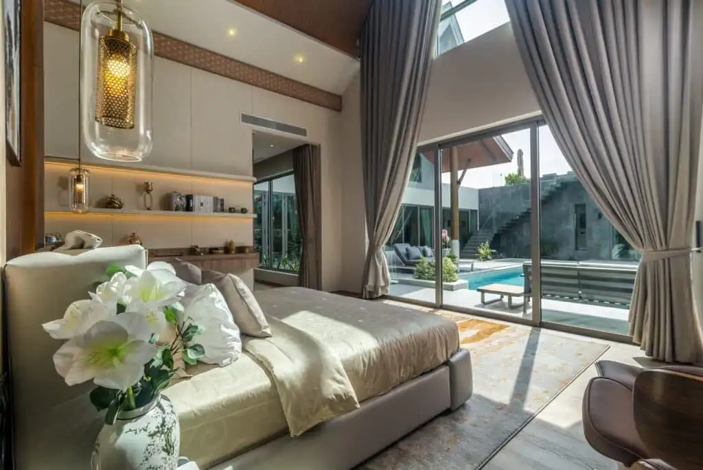 Luxurious bedroom with elegant decor, large windows, and pool view. Features stylish lighting and modern interior design.