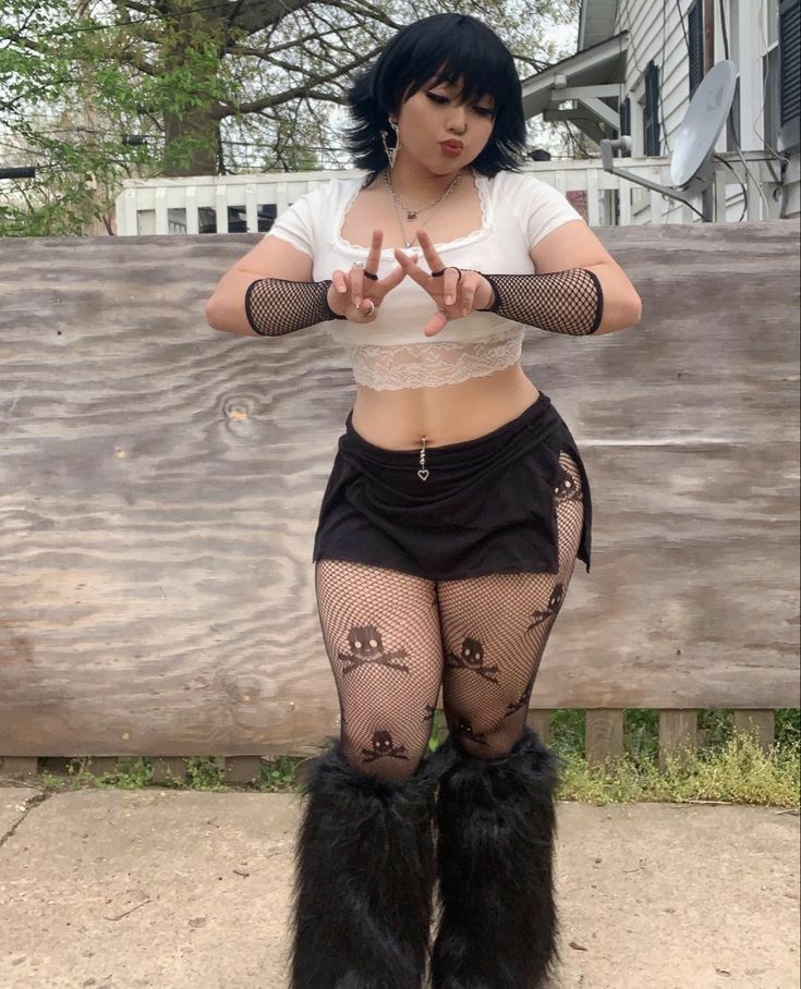 Plus Size Y2K Goth Rave Outfits Person in goth fashion with fishnet sleeves and leggings, white crop top, black skirt, and fluffy boots, posing outdoors. | Sky Rye Design Person in goth fashion with fishnet sleeves and leggings, white crop top, black skirt, and fluffy boots, posing outdoors.