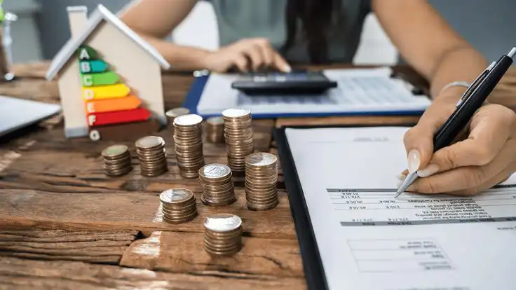 Coins stacked on a wooden table with energy efficiency chart and calculator, depicting cost management and savings in real estate.