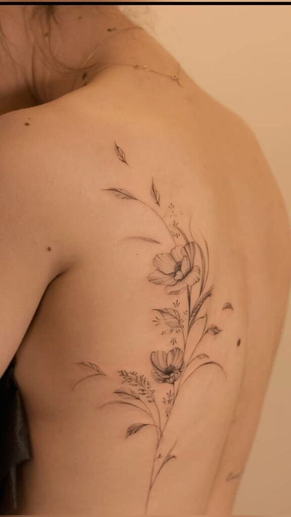 Delicate floral tattoo on a woman's back, featuring intricate line work and blooming flowers. Elegant body art design on skin.