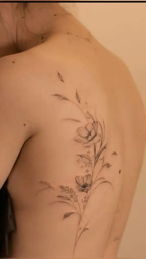 Delicate floral tattoo on a woman's back, featuring intricate line work and blooming flowers. Elegant body art design on skin.