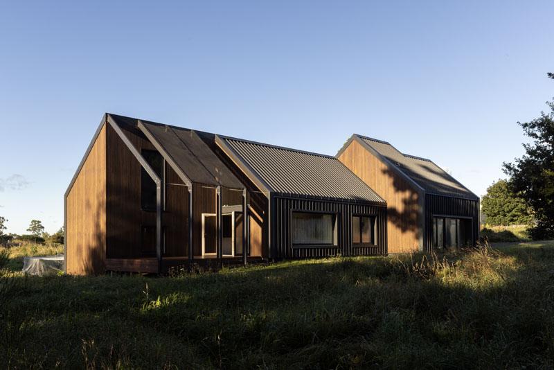 Modern wooden house with large windows in a grassy landscape under clear blue sky, showcasing contemporary architecture in nature.