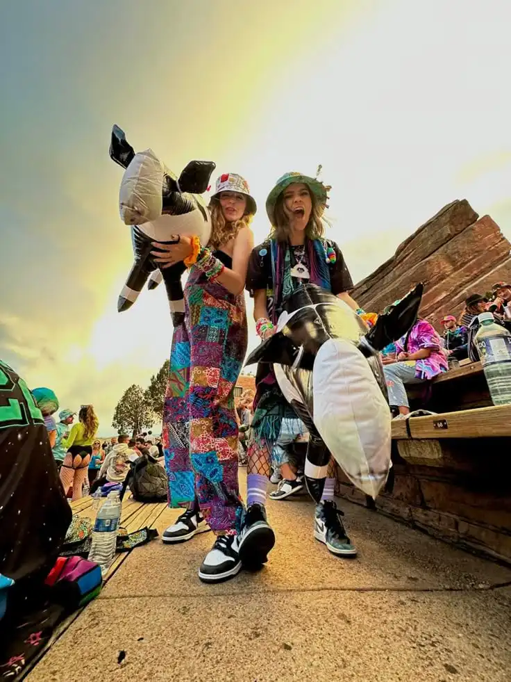 People in colorful outfits having fun with inflatables at an outdoor music festival.