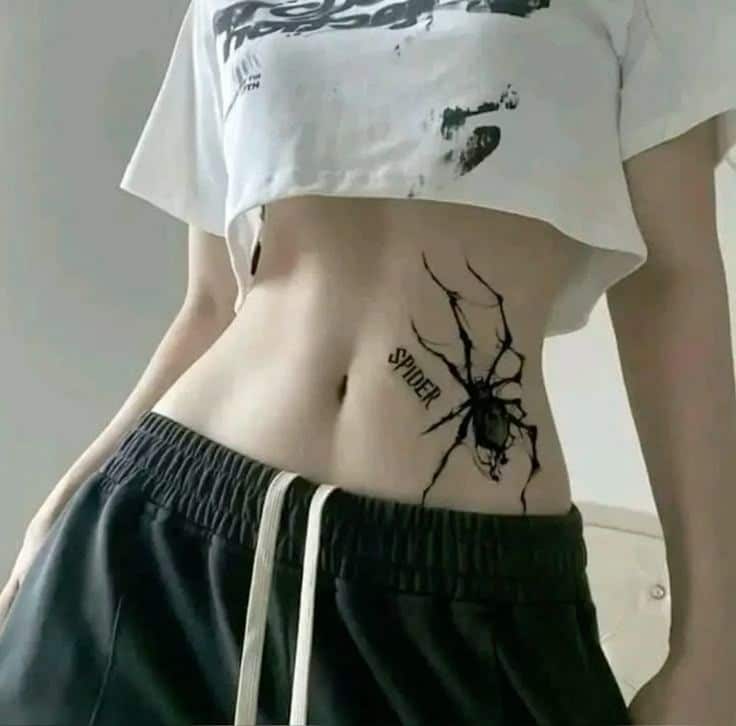 Realistic Black Spider Tattoo on Waist _ Horror-Inspired Ink for Women Person with a spider tattoo on their side, wearing a cropped t-shirt and joggers, showcasing unique body art. | Sky Rye Design Person with a spider tattoo on their side, wearing a cropped t-shirt and joggers, showcasing unique body art.