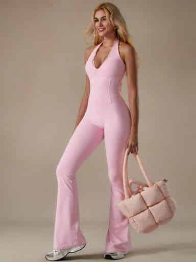 SHEIN Smiling woman in a pink halter jumpsuit holding a matching quilted bag, standing against a beige background. Fashion and style concept. | Sky Rye Design Smiling woman in a pink halter jumpsuit holding a matching quilted bag, standing against a beige background. Fashion and style concept.