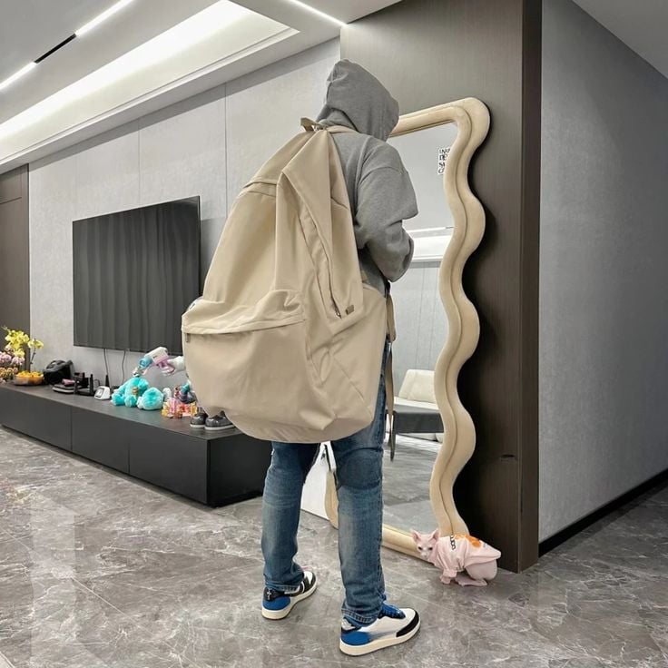 Sac à dos pour voyage super grand et aéré angiBackpack Person in hoodie with oversized backpack looks in wavy mirror, standing on marble floor beside a modern TV unit with | Sky Rye Design Person in hoodie with oversized backpack looks in wavy mirror, standing on marble floor beside a modern TV unit with