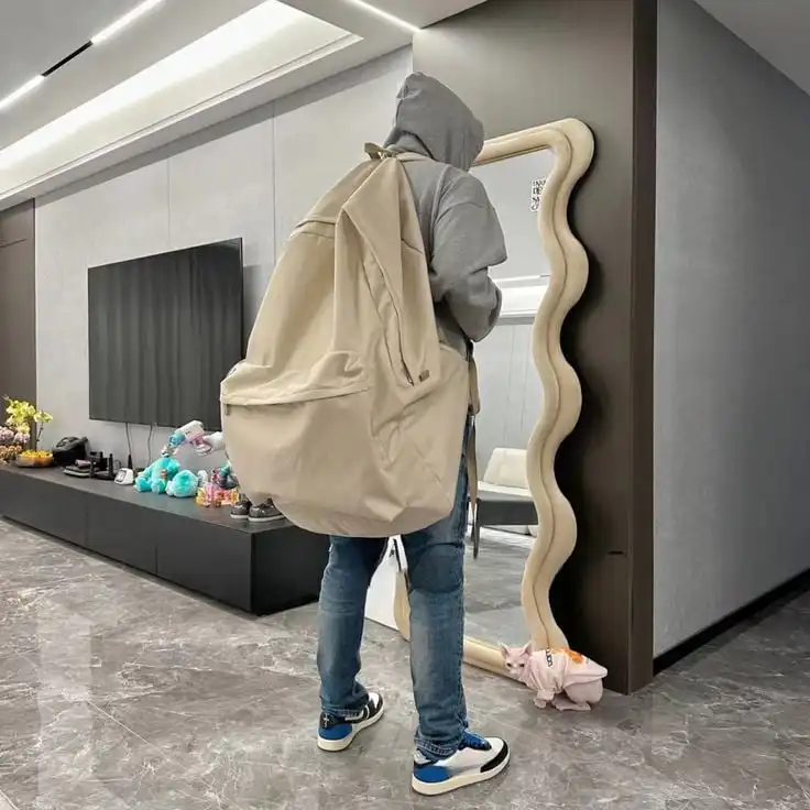 Person in hoodie with oversized backpack looks in wavy mirror, standing on marble floor beside a modern TV unit with