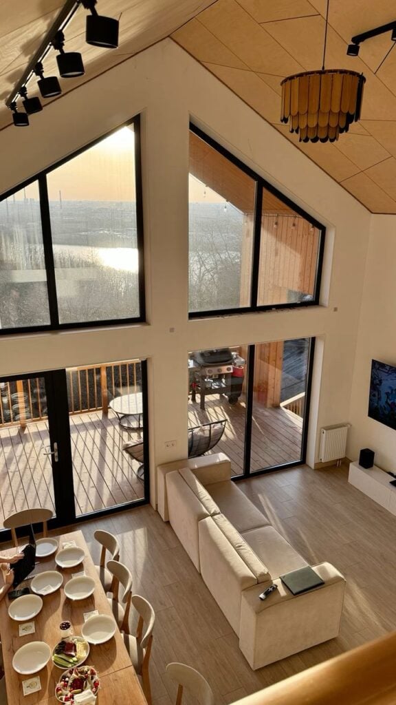 Spacious modern living room with large windows overlooking a scenic sunset, featuring cozy furniture and a dining table setup.