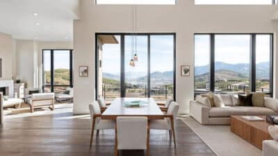 Modern open-concept living space with large windows offering scenic mountain views, featuring a dining table, cozy sofas, and natural light.