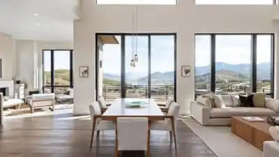 Modern open-concept living space with large windows offering scenic mountain views, featuring a dining table, cozy sofas, and natural light.