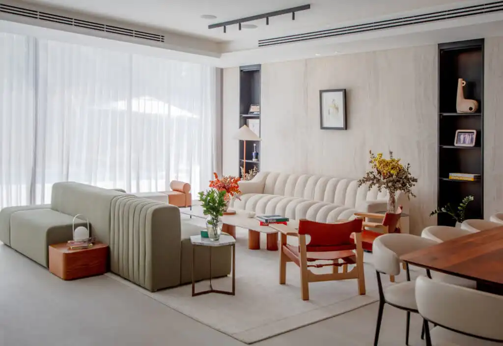 Modern living room with chic furniture, featuring a cozy beige sofa, stylish chairs, and elegant decor against sheer curtains.