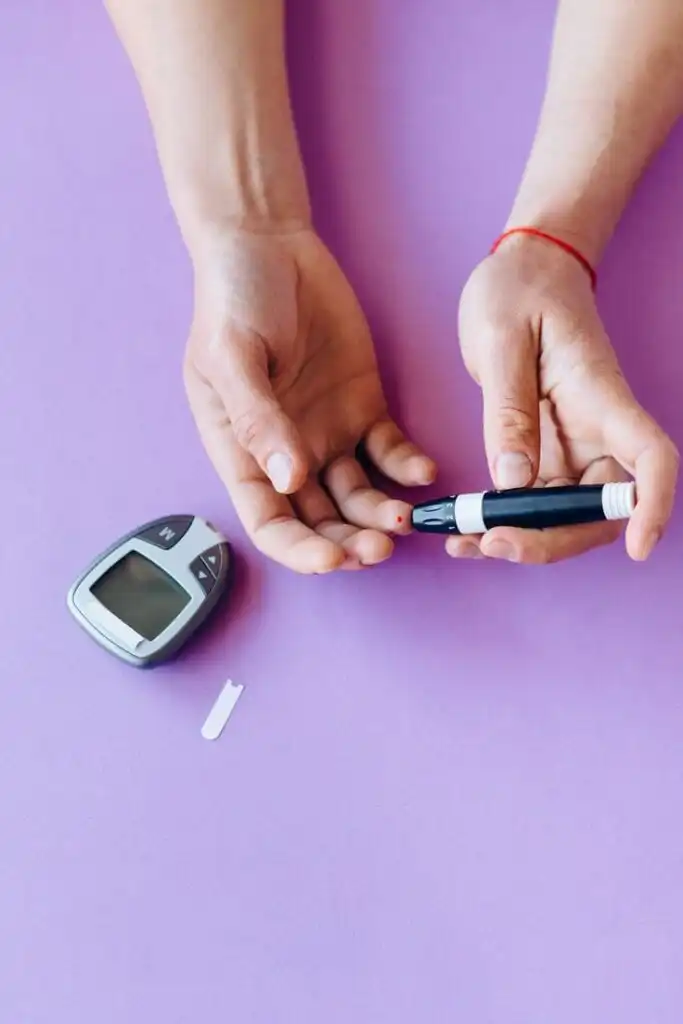 Person checking blood sugar with glucometer and lancet on a purple background, emphasizing diabetes management.