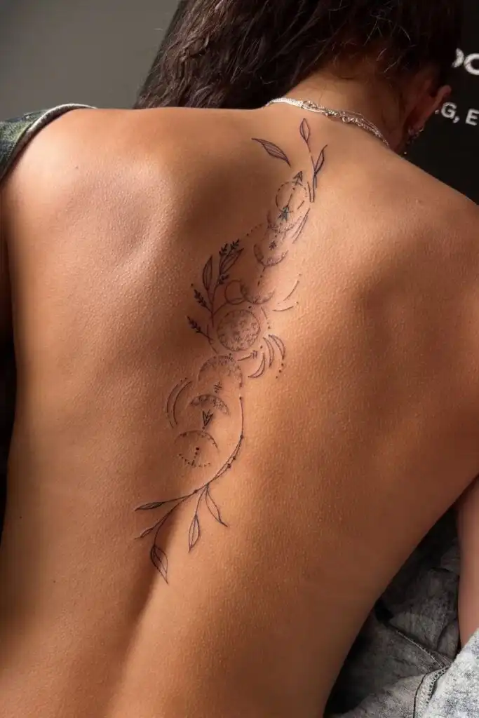 Back tattoo with floral and moon phases design, showcasing intricate line work on skin. Elegant and artistic body art concept.