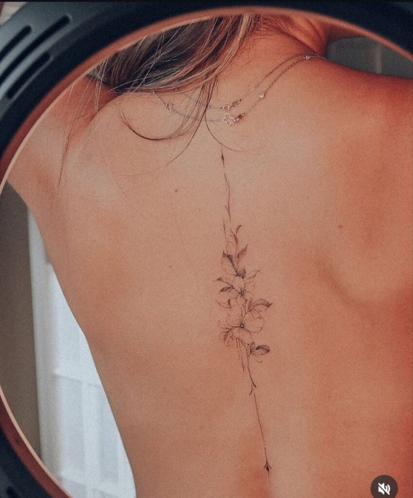 Delicate floral tattoo on the upper back, showcasing intricate leaf and flower detail, under soft lighting.
