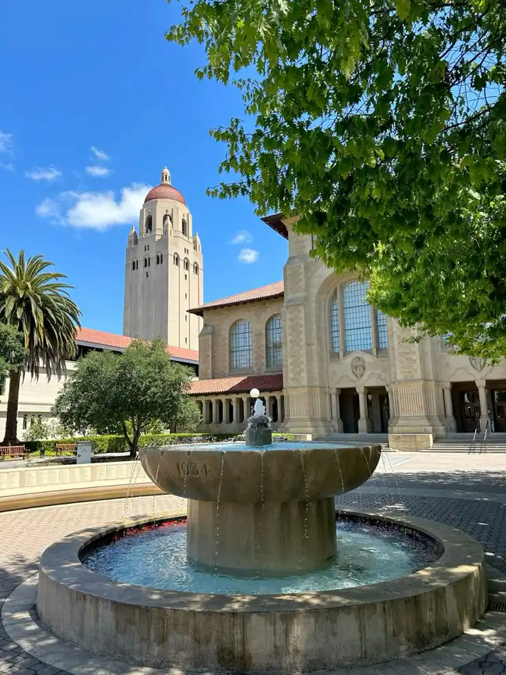 Historic tower and fountain with scenic architecture, surrounded by greenery and blue skies, perfect for exploring cultural landmarks.