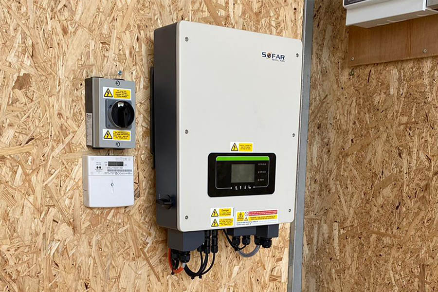Wall-mounted solar power inverter with control panel and safety switches, installed on wooden paneling in an industrial