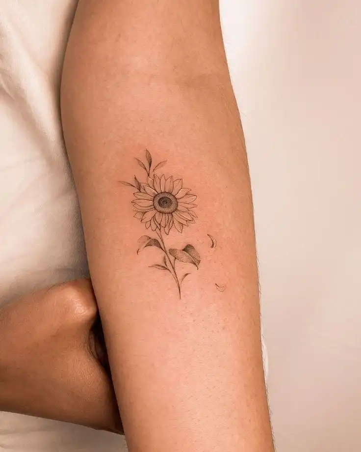Minimalist sunflower tattoo on forearm, showcasing delicate petals and leaves for a unique floral design. Ideal for tattoo inspiration.