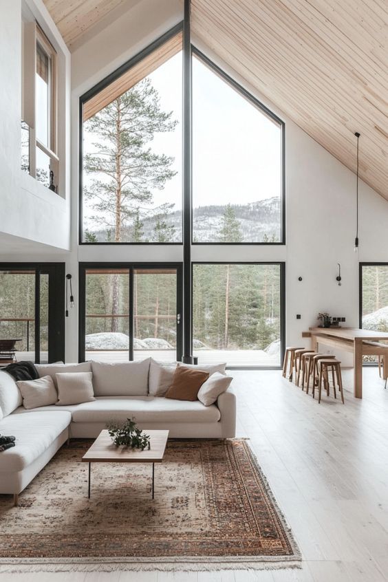 Modern Scandinavian living room with large windows, wooden ceiling, cozy sofa, and natural views. Bright, minimalist interior design.