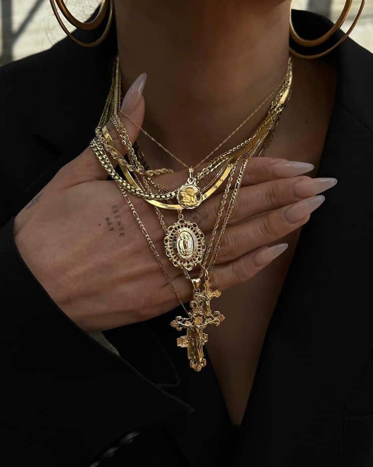 Stylish layered gold necklaces and hoop earrings, paired with elegant long nails on person in a black outfit.