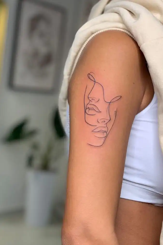 Minimalist line art face tattoo on woman's upper arm, stylishly showcasing unique body art.