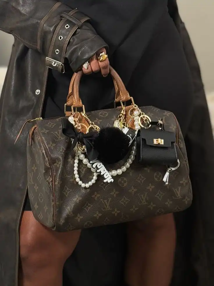 Luxurious monogram handbag adorned with pearl and charm accessories, held by a person dressed in stylish black leather outfit.