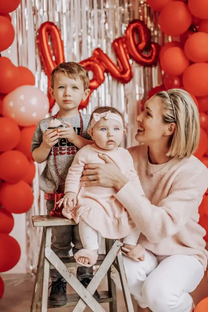 Valentines Day shoot with the girls and the kids - Fashion and my Fellows Mother with two children at a festive celebration with red balloons and love decoration, toddler holding a cupcake, creating a joyful scene. | Sky Rye Design Mother with two children at a festive celebration with red balloons and love decoration, toddler holding a cupcake, creating a joyful scene.