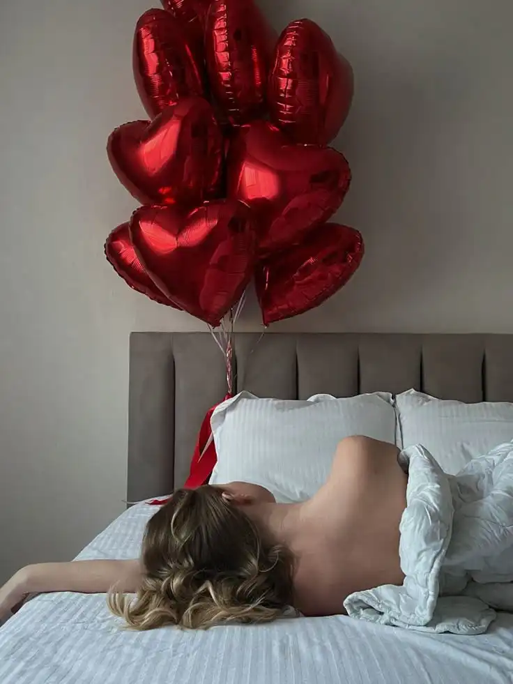 Valentines Day ♥️ Woman lying in bed under white sheets with red heart-shaped balloons floating above, creating a romantic and serene atmosphere. | Sky Rye Design Woman lying in bed under white sheets with red heart-shaped balloons floating above, creating a romantic and serene atmosphere.